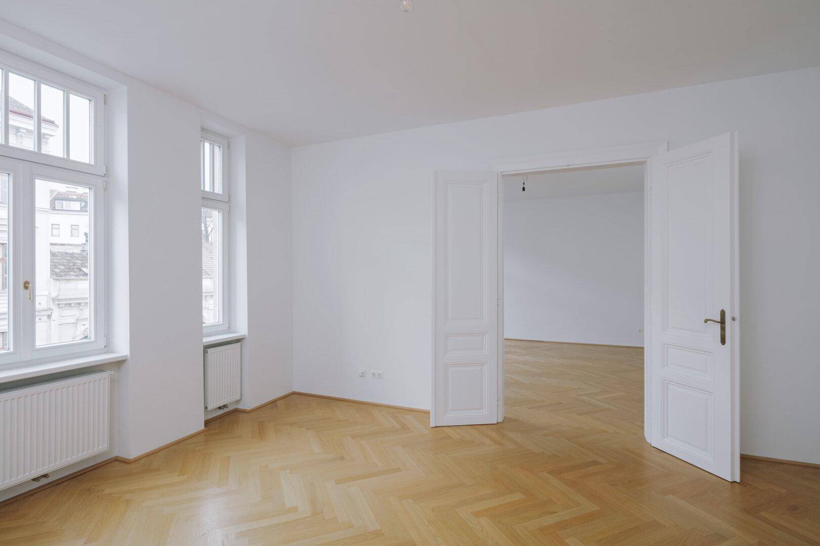 Geräumiges, helles Zimmer mit klassischem Fischgrätparkett und großen Fenstern.