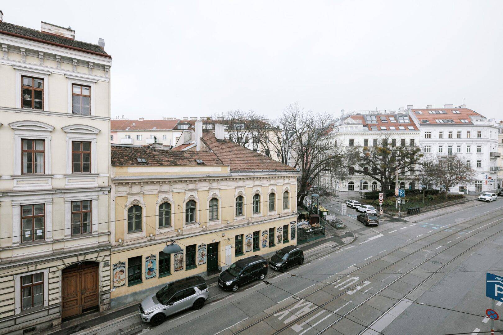 Blick von oben auf eine belebte Straße mit historischen Gebäuden und Straßenbahnschienen.