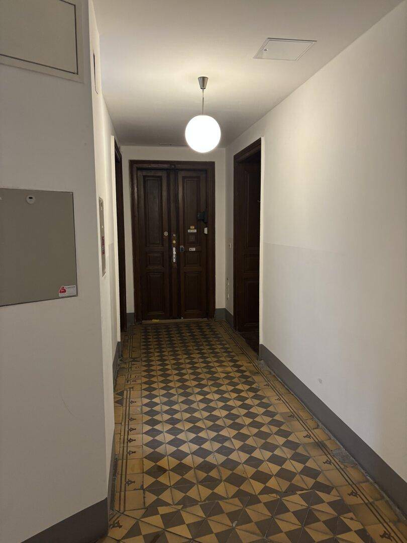 Langer Flur mit gemusterten Fliesen und dunklen Holztüren.