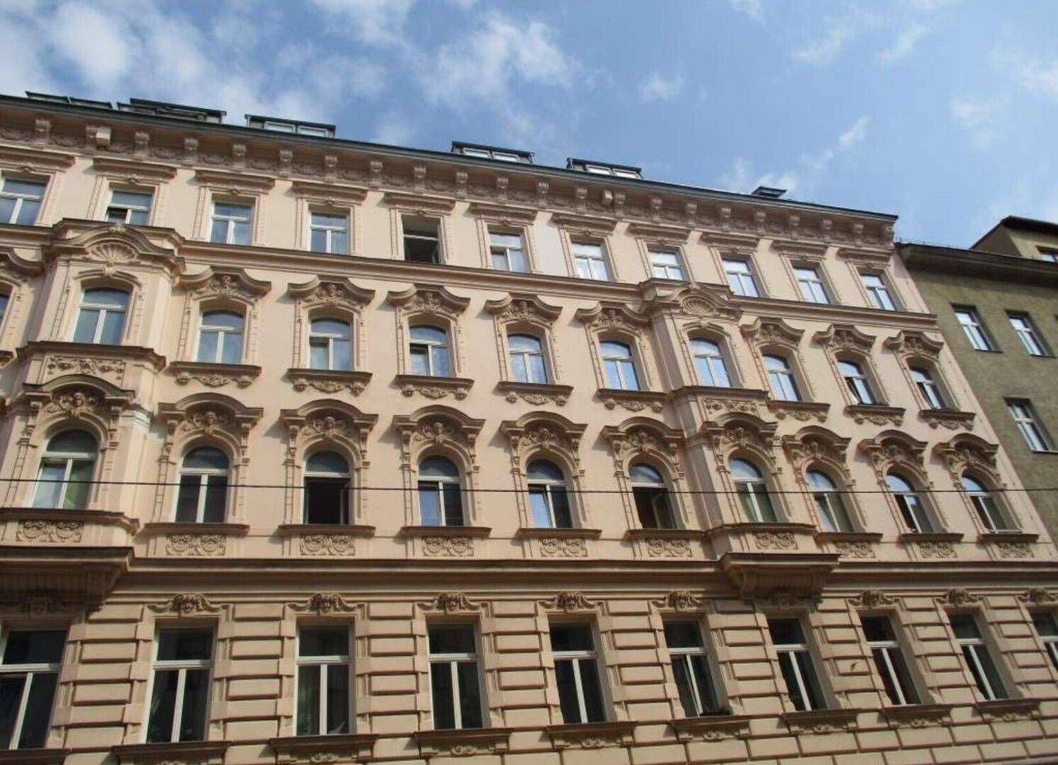 Historische Fassade eines Altbaus mit reich verzierten Fenstern und Balkonen.