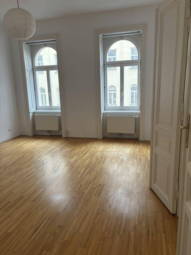 Geräumiges Zimmer mit klassischem Parkettboden, hohen Decken und großen Fenstern.