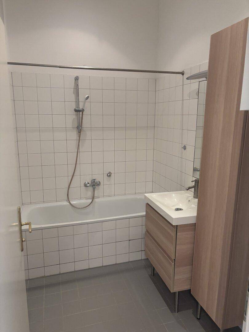 Modernes Badezimmer mit Badewanne, weißen Wandfliesen und einem Holzwaschtisch.