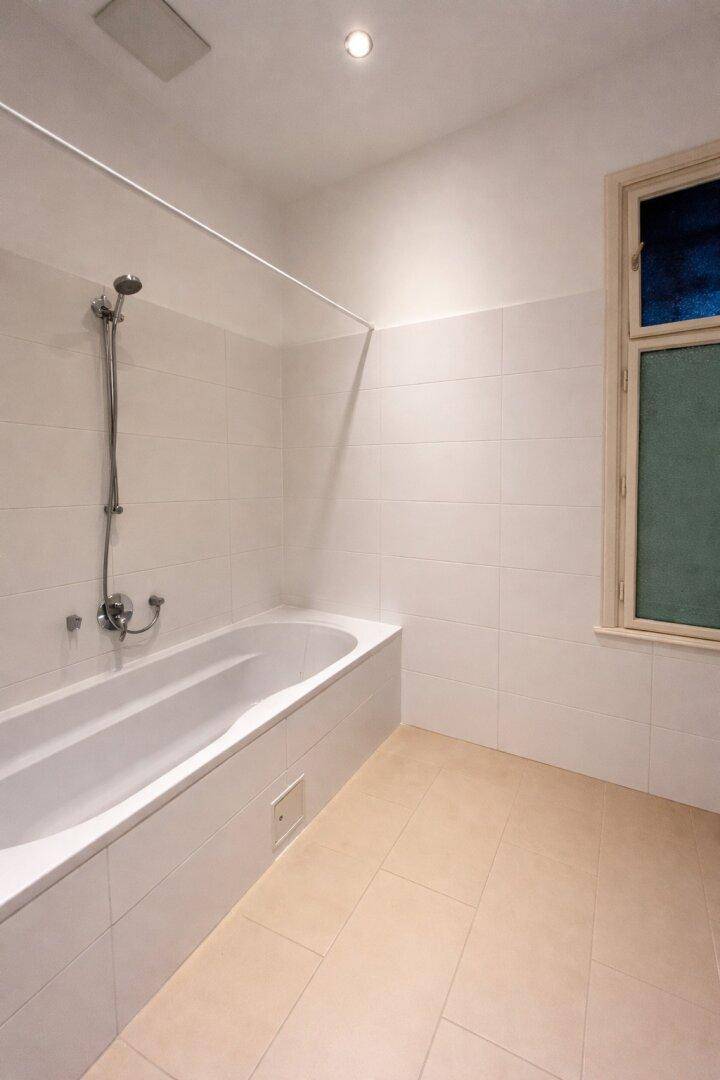 Helles Badezimmer mit Badewanne, weißen Fliesen und einem Fenster für Tageslicht und Belüftung.