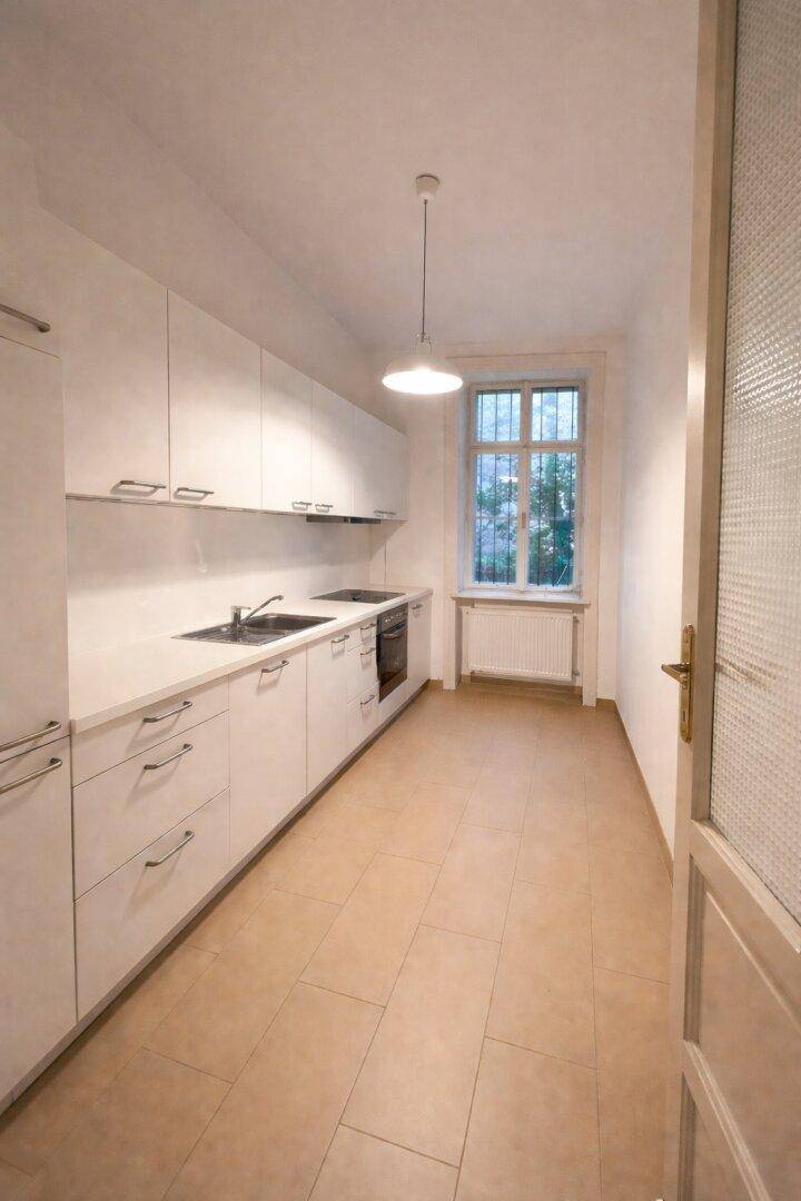 Moderne Einbauküche mit weißen Schränken, Fliesenboden und einem Fenster für natürliche Belüftung.