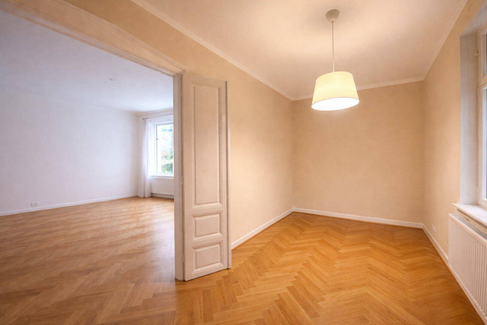 Geräumiges Zimmer mit Fischgrätparkett und einer Verbindungstür zu einem angrenzenden Bereich.