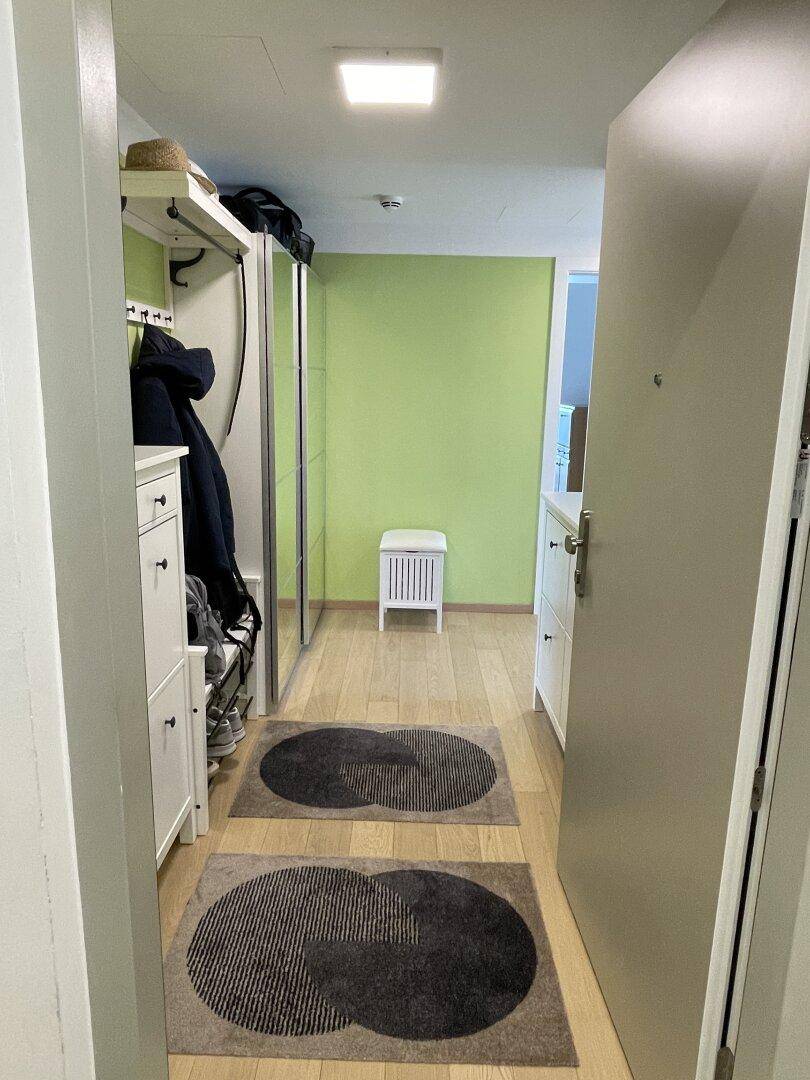 Heller Flur mit Garderobe, Spiegel und einer auffälligen grünen Akzentwand, einladend gestaltet.