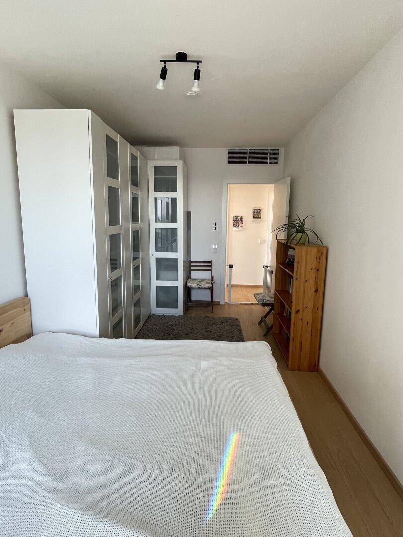 Helles Schlafzimmer mit großem Bett und geräumigem weißen Kleiderschrank, ergänzt durch einen Teppich.