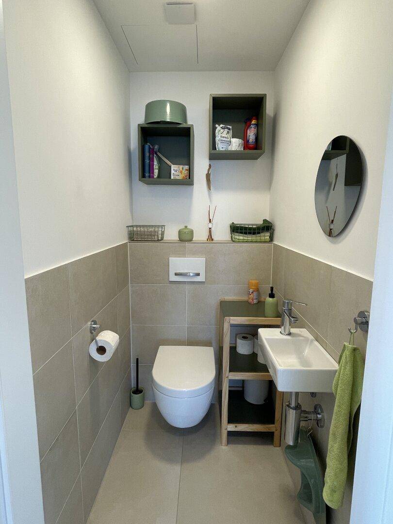 Modernes Gäste-WC mit wandhängender Toilette, kleinem Waschbecken und hellen Fliesen an Wänden und Boden.
