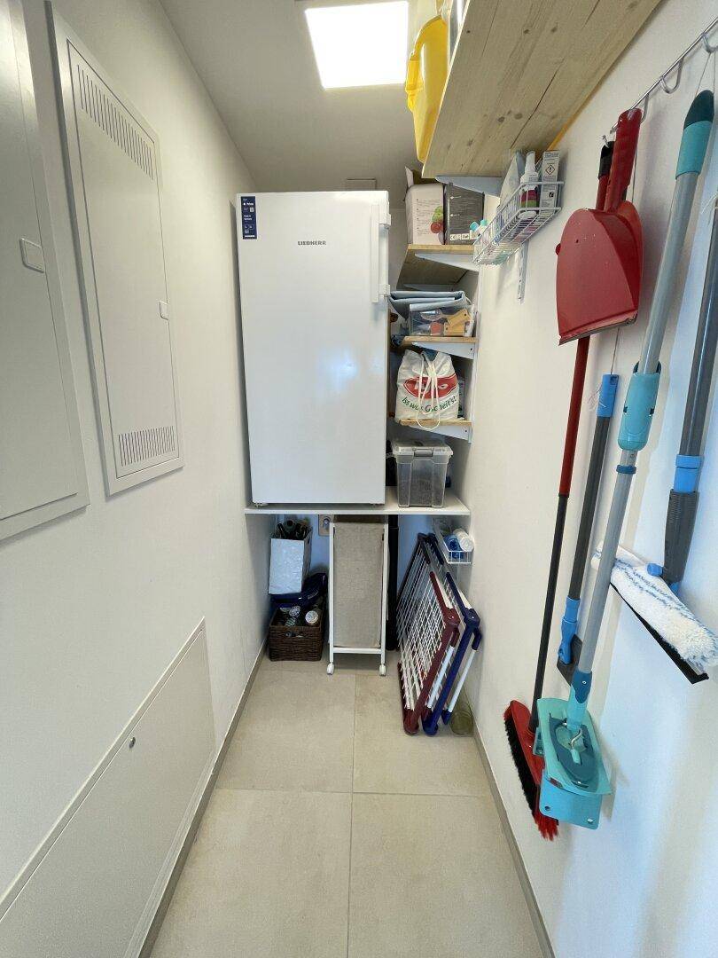 Praktischer Hauswirtschaftsraum mit Kühlschrank, Regalen und Stauraum für Reinigungsutensilien.