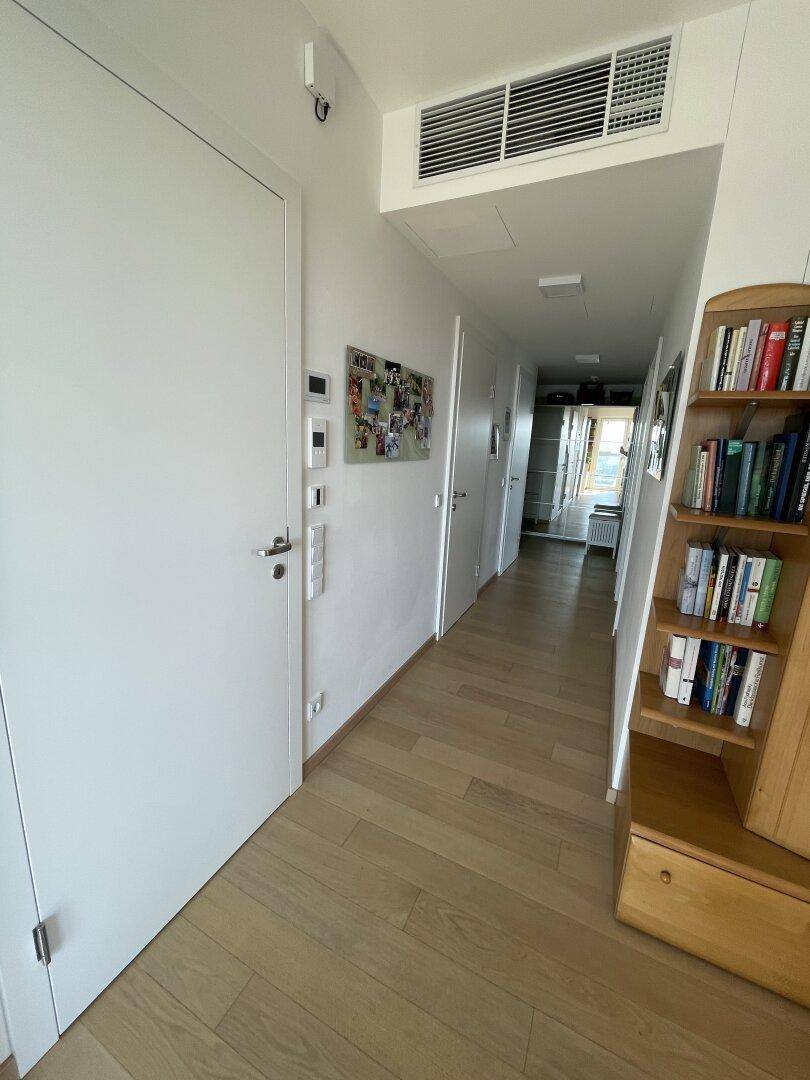 Langer Flur mit hellem Holzboden, weißen Türen und einem Bücherregal, gut beleuchtet.
