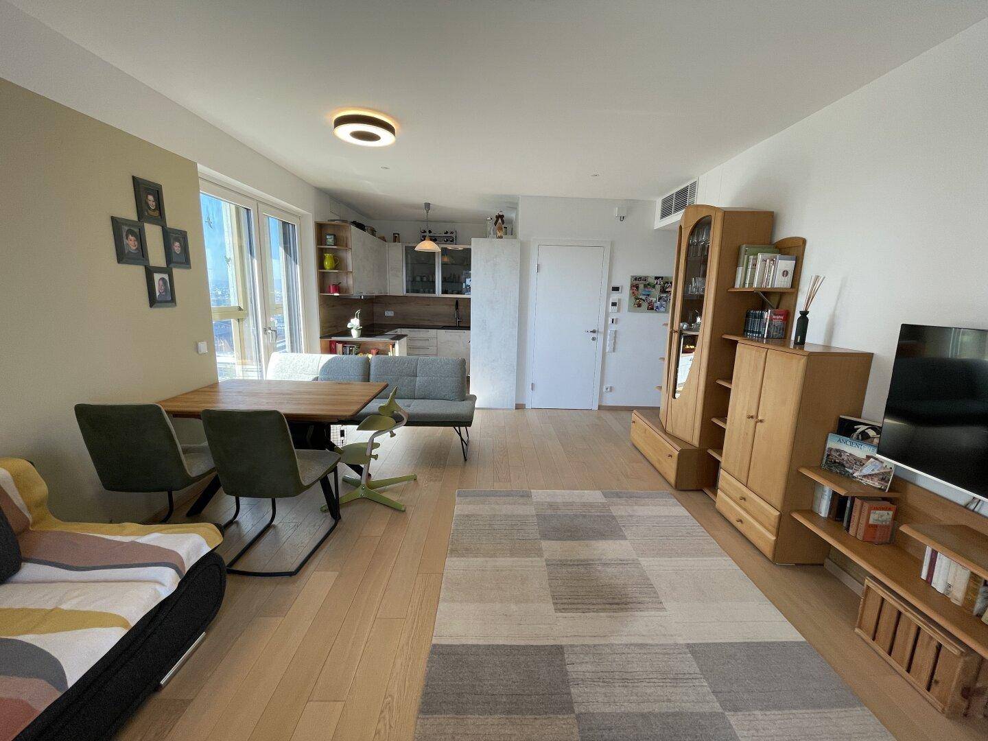 Heller Wohnbereich mit Esstisch, Sofa und integrierter Küche, ausgestattet mit Holzboden und Teppich.