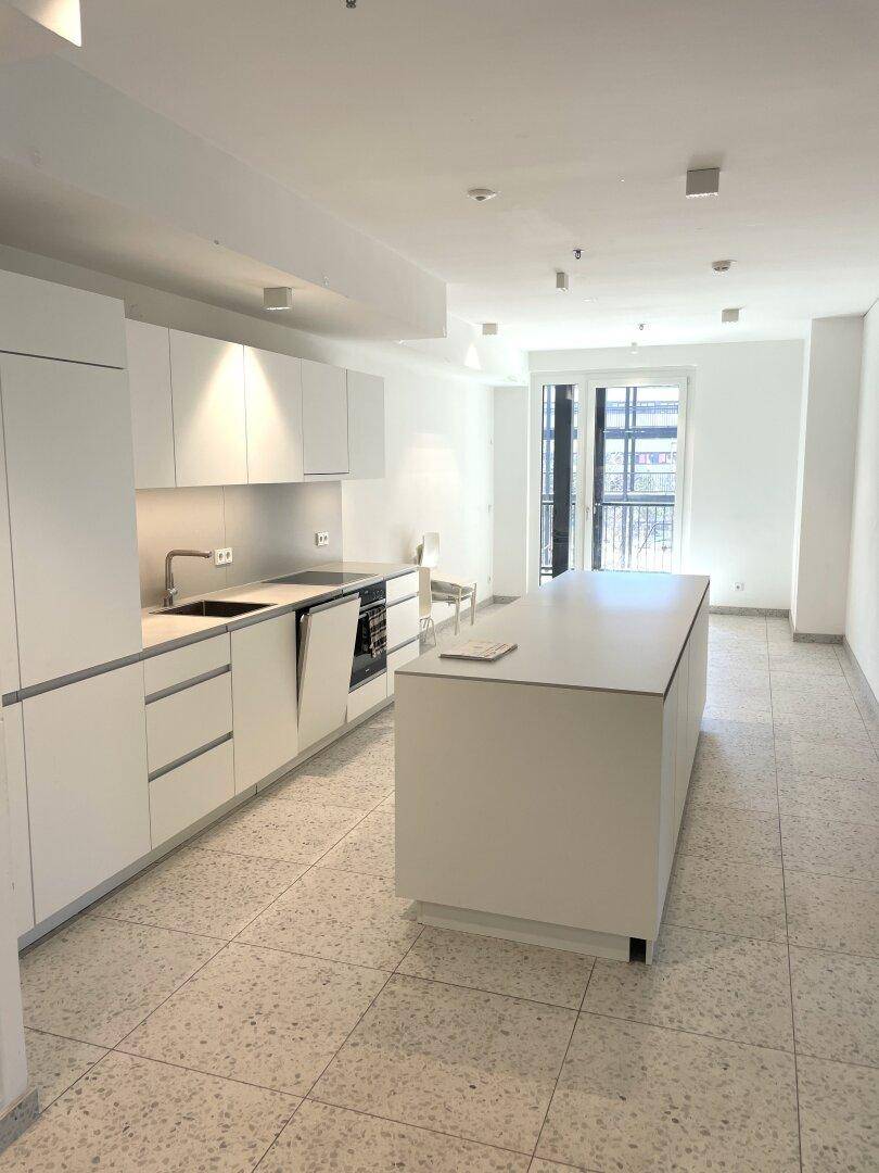Moderne, unmöblierte Küche mit weißen Schränken, Kücheninsel und Zugang zu einem Balkon.