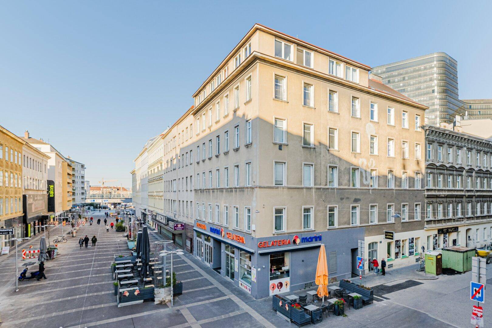 Historisches Gebäude an einer belebten Straße mit Geschäften im Erdgeschoss.