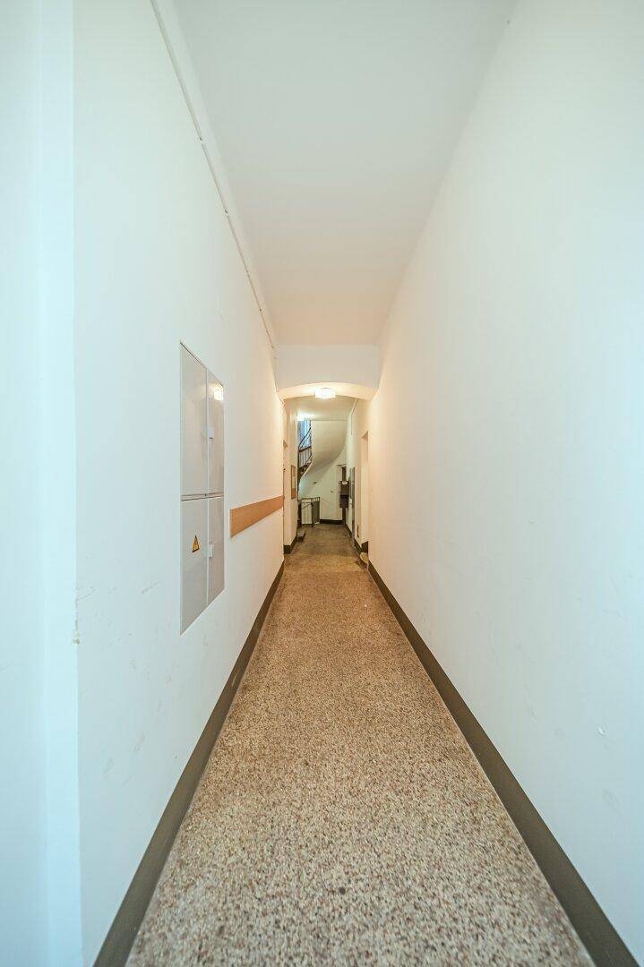 Langer, schmaler Flur mit Terrazzoboden und weißen Wänden in einem Altbau.