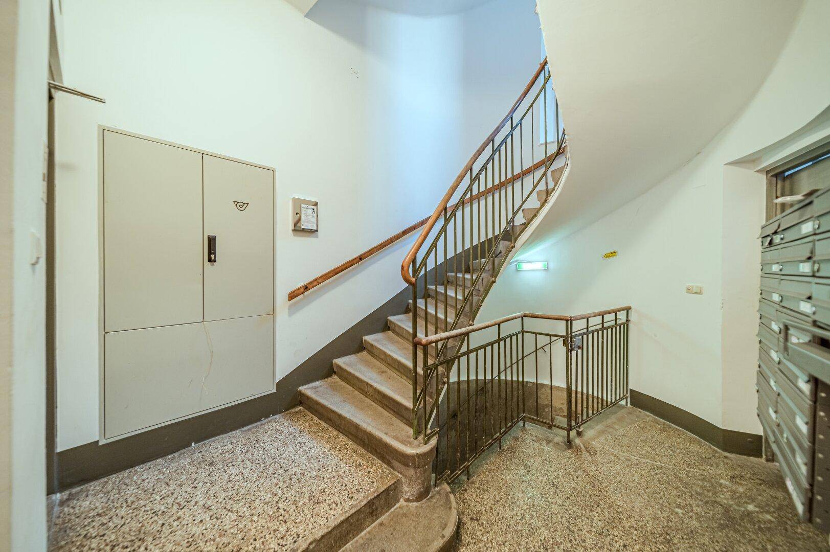 Geschwungenes Treppenhaus mit Metallgeländer und Terrazzoboden in einem Altbau.