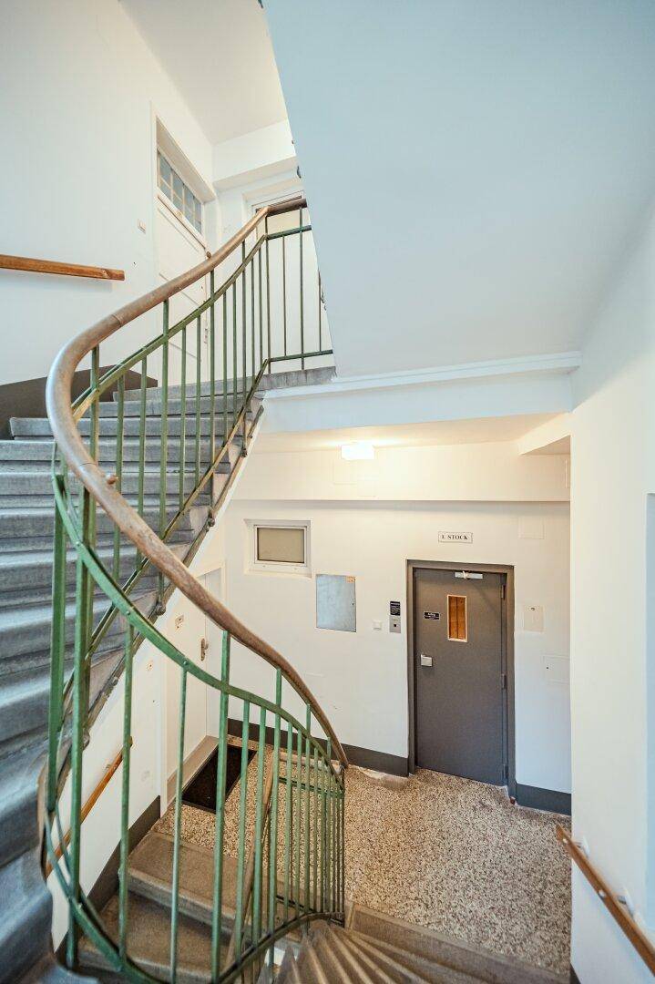 Treppenhaus mit geschwungenem Geländer und Zugang zum Aufzug in einem Mehrfamilienhaus.