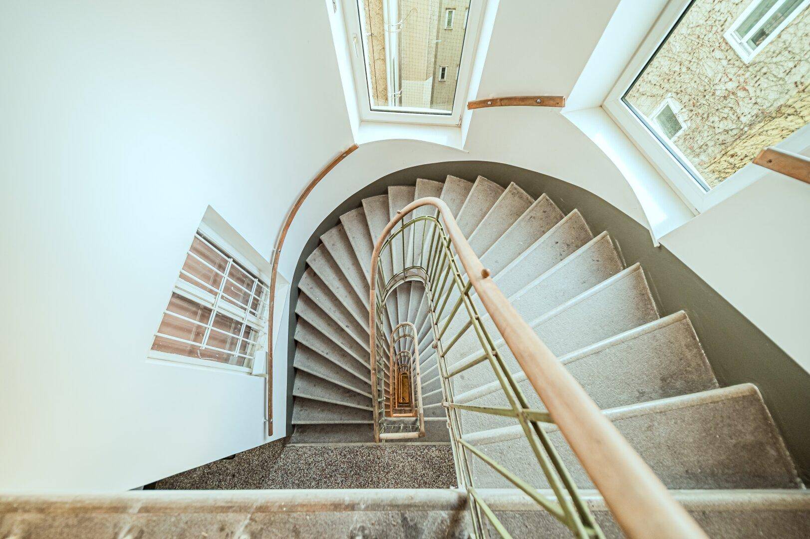 Blick von oben auf ein elegantes, geschwungenes Treppenhaus mit viel Tageslicht.