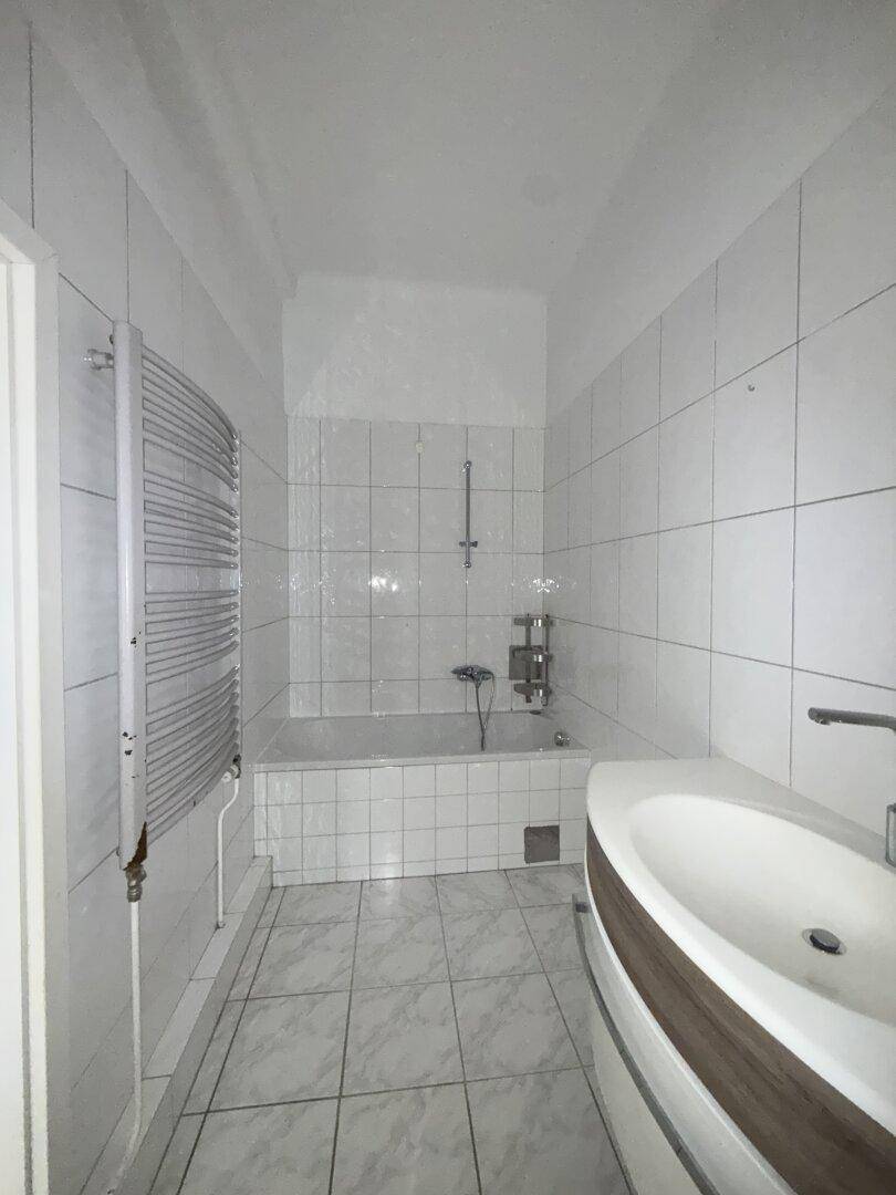 Gefliestes Badezimmer mit Badewanne, modernem Waschbecken und beheiztem Handtuchhalter.
