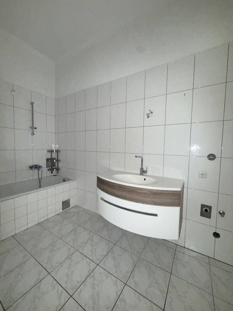 Helles Badezimmer mit weißen Fliesen, modernem Waschbecken und Platz für eine Waschmaschine.