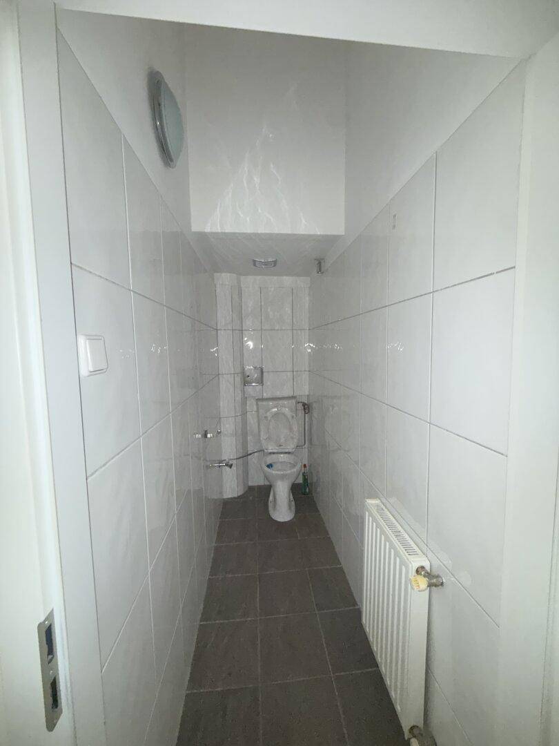 Schmale, weiß geflieste Gästetoilette mit WC und Heizkörper, funktional und sauber.