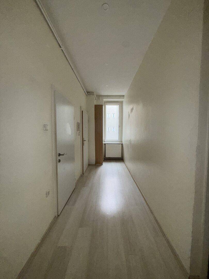 Heller Flur mit Parkettboden, einem Fenster am Ende und Zugang zu weiteren Räumen.