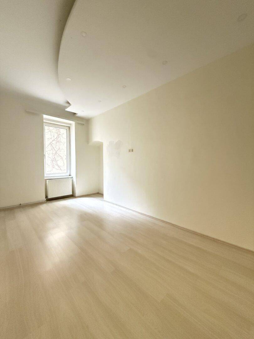 Geräumiges, helles Zimmer mit Parkettboden und einem Fenster, ideal für Wohn- oder Schlafbereich.