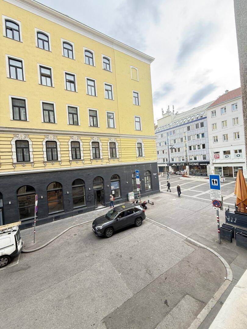 Blick aus dem Fenster auf eine belebte Stadtstraße mit historischen Gebäuden und parkenden Autos.
