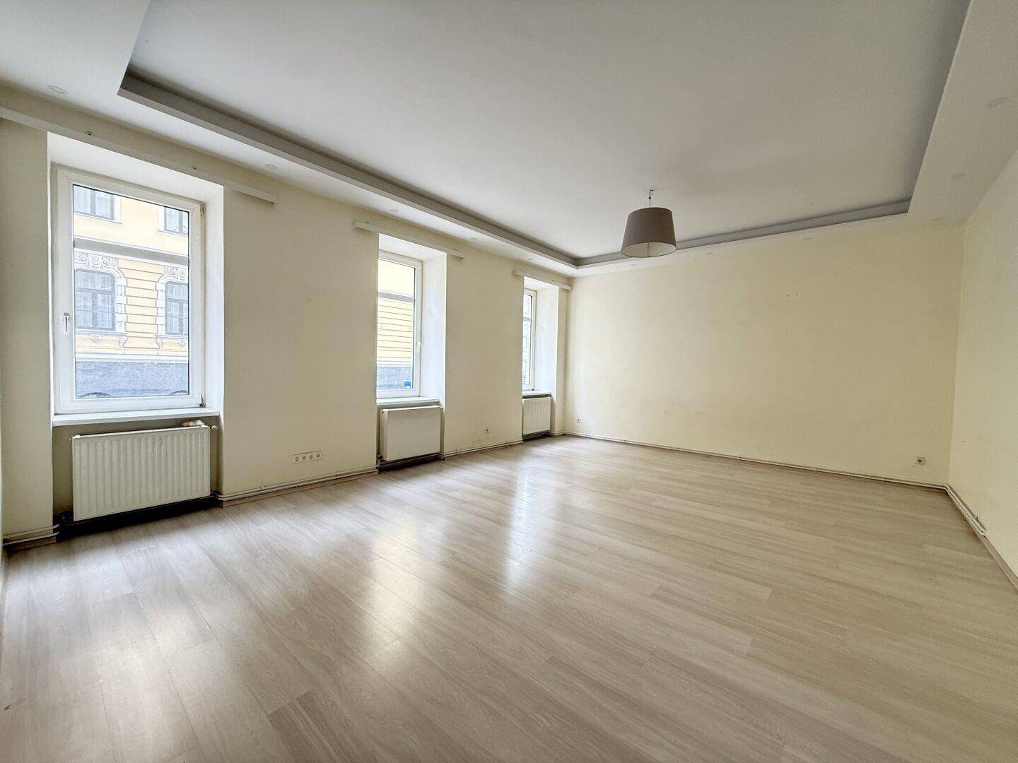 Helles, leeres Zimmer mit Parkettboden und mehreren Fenstern, bereit zur individuellen Gestaltung.