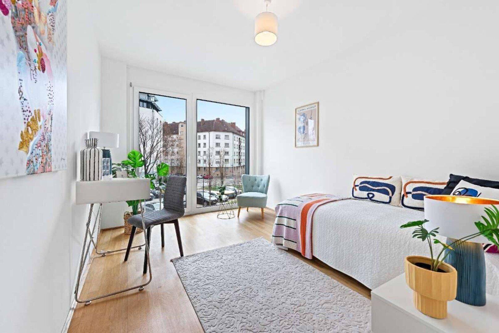 Helles Schlafzimmer mit Holzboden, Schreibtisch und großen Fenstern mit Blick auf die Stadt.