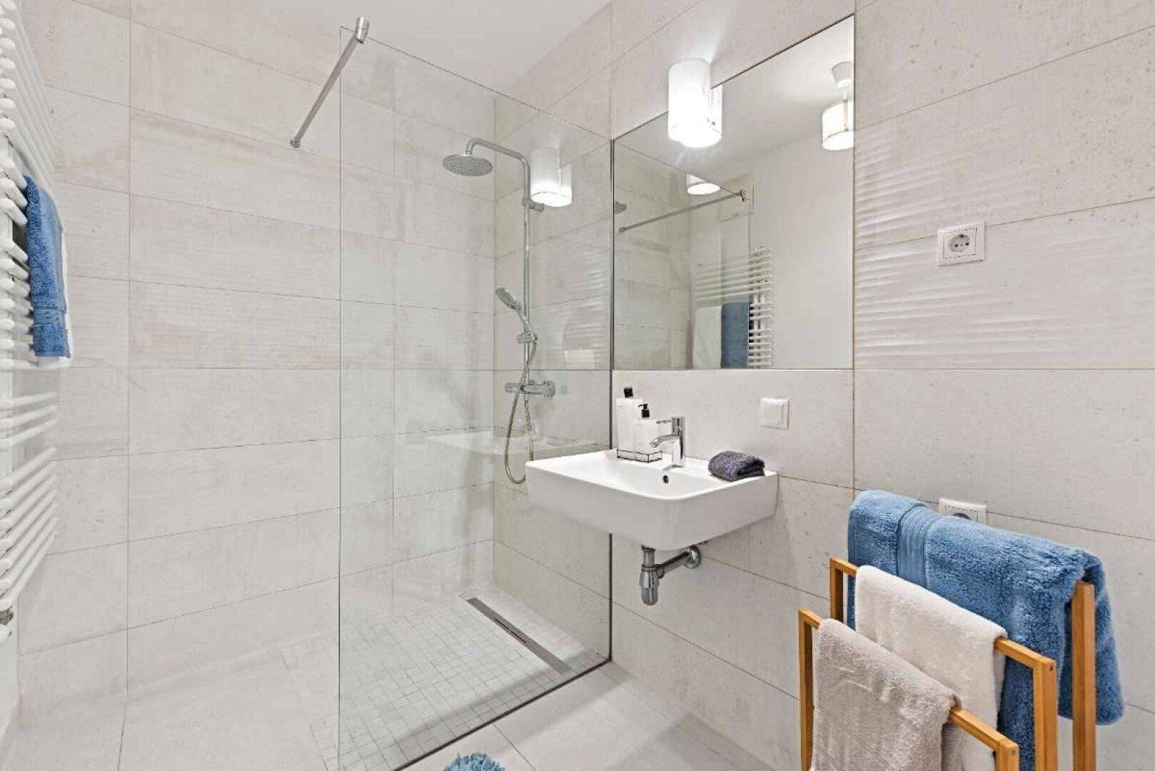 Modernes Badezimmer mit begehbarer Dusche, weißen Fliesen und praktischem Handtuchheizkörper.