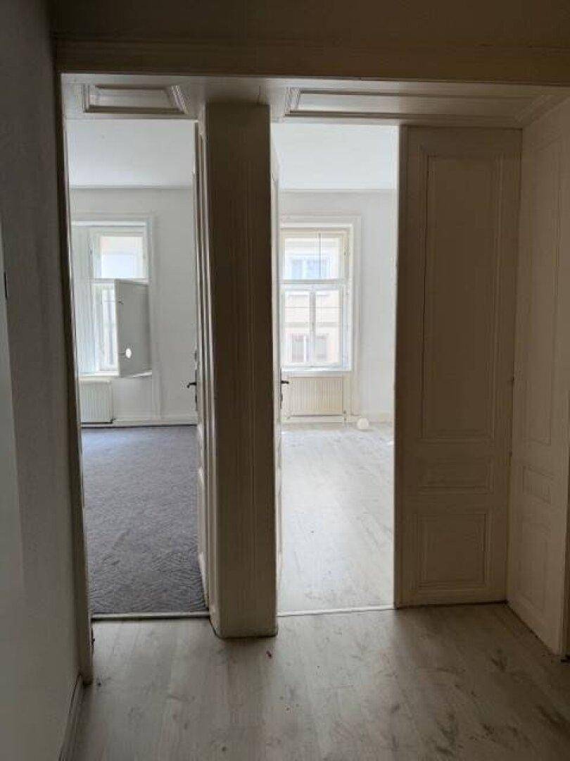 Blick durch eine Türöffnung in zwei separate, helle Zimmer mit unterschiedlichen Bodenbelägen.