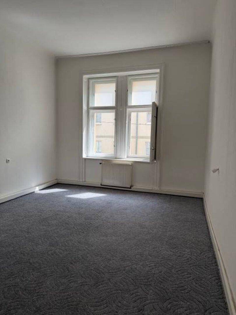 Gemütliches Zimmer mit dunklem Teppichboden und einem großen Fenster für natürliche Belichtung.