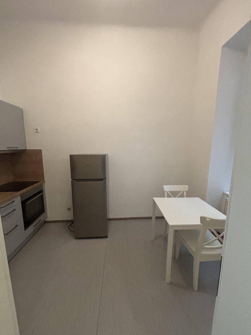 Einfache Küche mit Einbauschränken, Kühlschrank und einem kleinen Esstisch für zwei Personen.