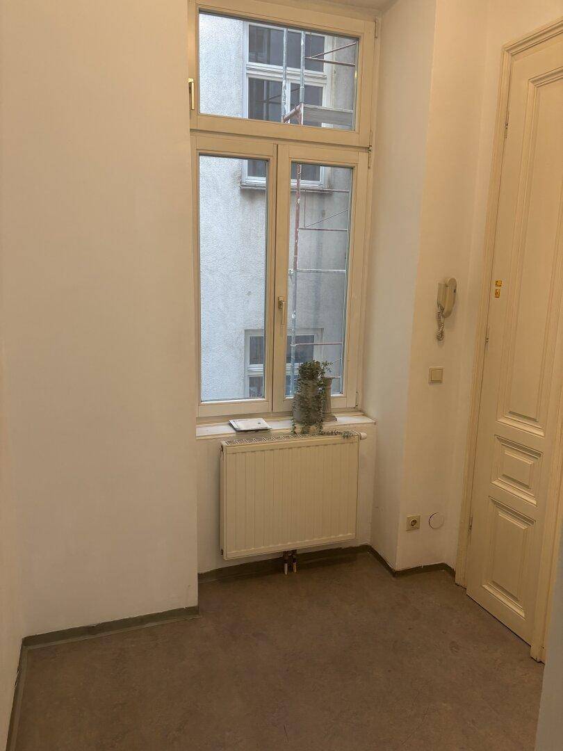 Heller Flur mit einem Fenster und Heizkörper, der einen Blick auf den Innenhof bietet.