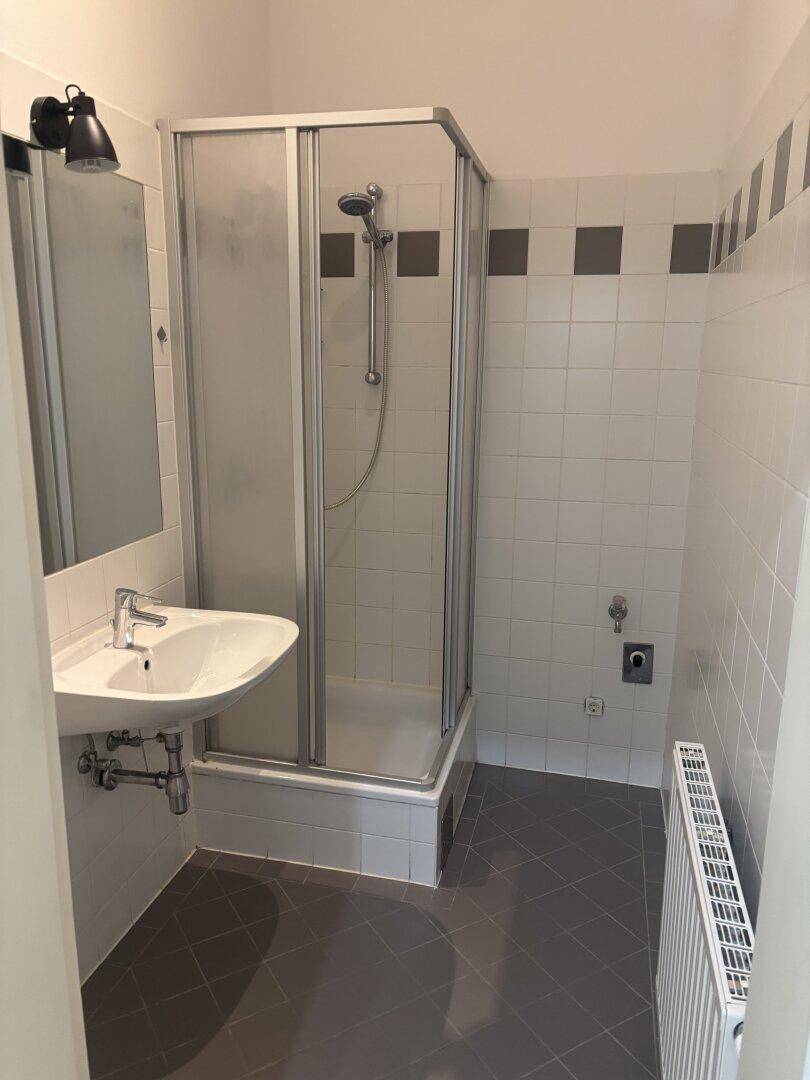 Funktionales Badezimmer mit Duschkabine, Waschbecken und Fliesen in Weiß und Grau.