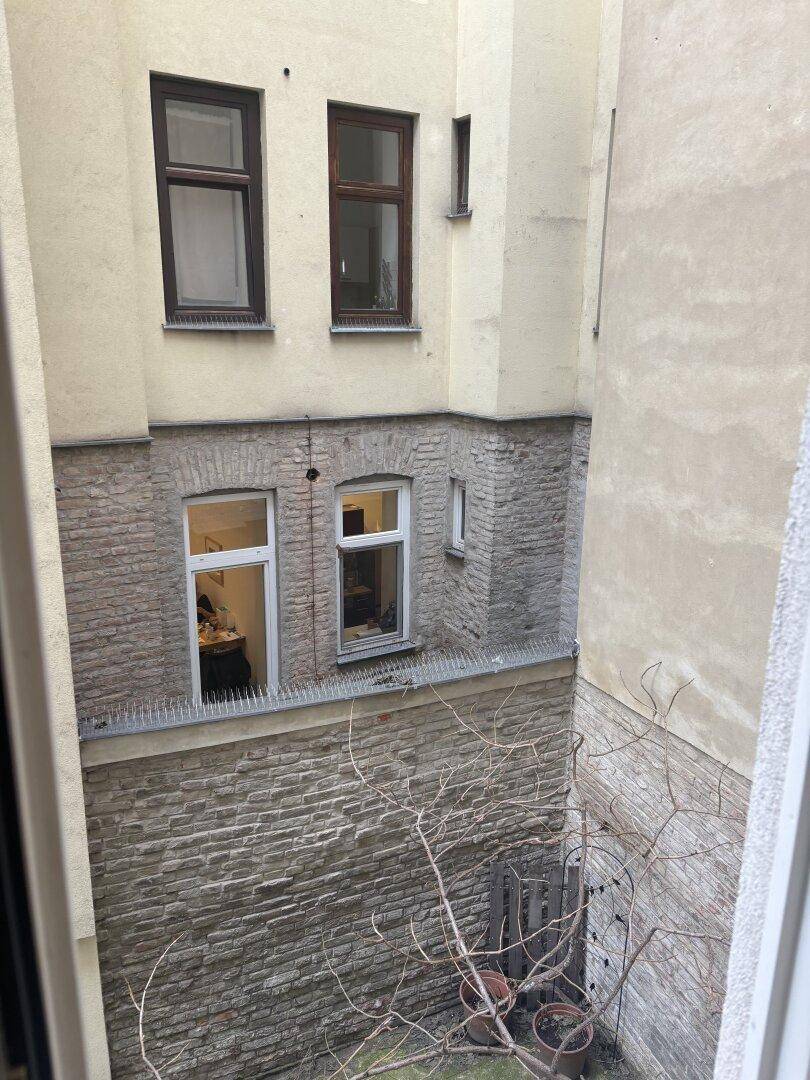 Blick aus dem Fenster auf einen ruhigen Innenhof mit Backsteinwänden und wenig Vegetation.
