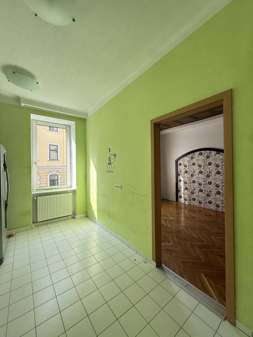 Helle Küche mit grünen Wänden, Fliesenboden und Fenster mit Blick auf die Stadt.