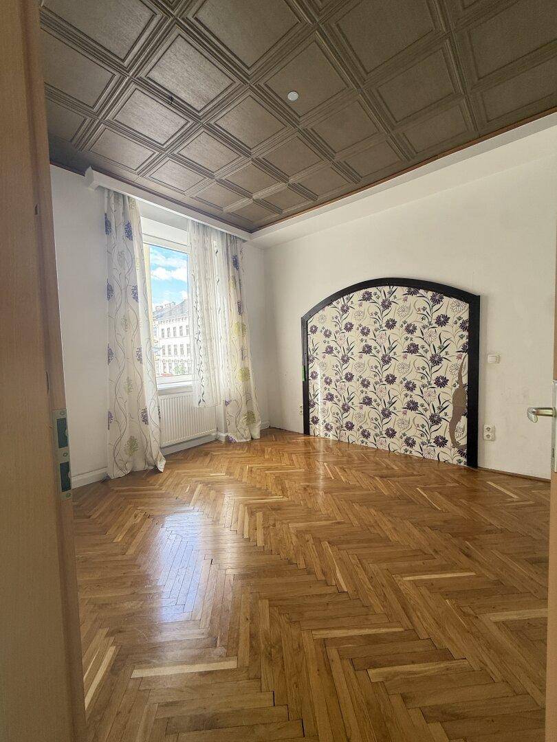 Geräumiges Zimmer mit Fischgrätparkett, dekorativer Decke und gemusterter Wandgestaltung.