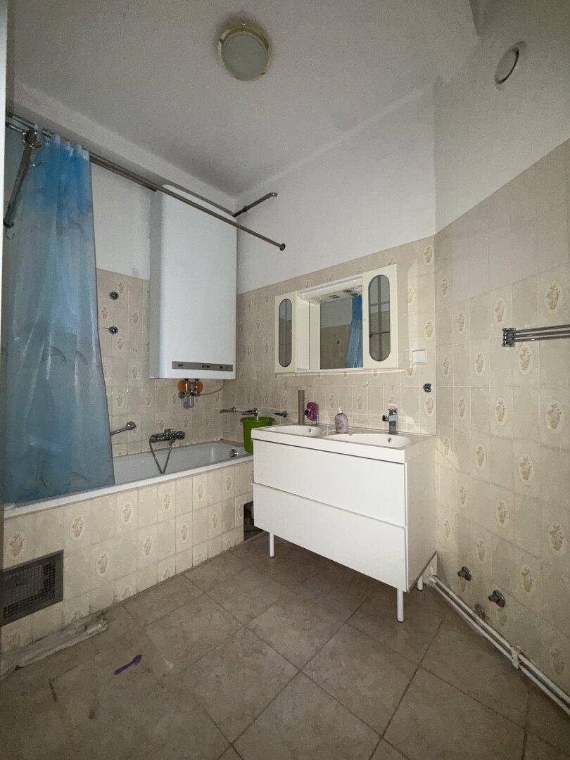 Badezimmer mit Badewanne, Waschbecken und beigen Fliesen, ausgestattet mit einem Spiegelschrank.