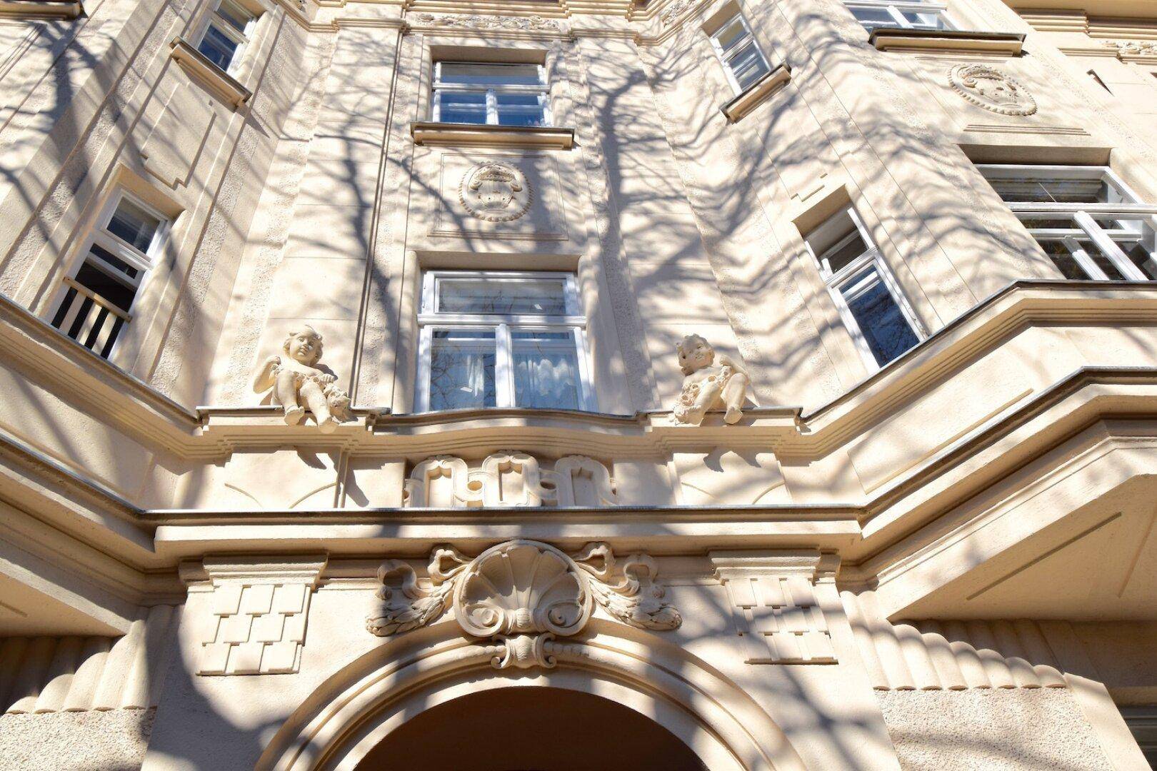 Detailaufnahme der Altbaufassade mit dekorativen Stuckelementen und kleinen Statuen über dem Eingang.