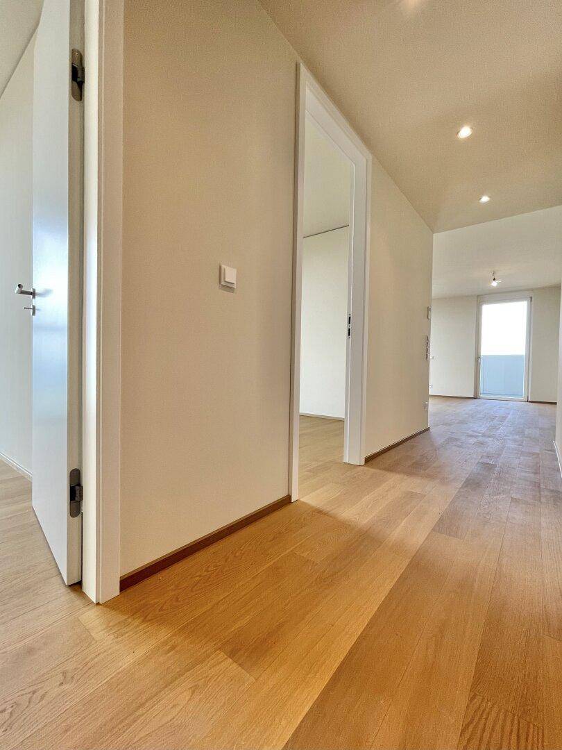 Heller Flur mit Holzboden und weißen Wänden, der zu verschiedenen Räumen führt.