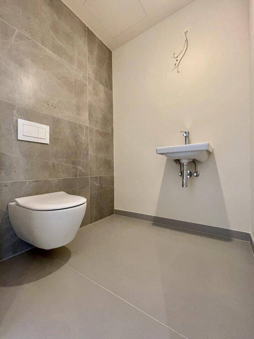 Modernes Gäste-WC mit wandhängender Toilette, kleinem Waschbecken und grauen Fliesen.