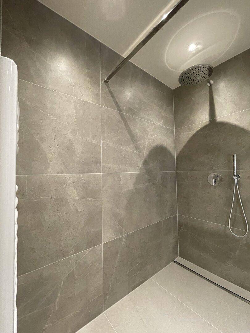 Geräumige begehbare Dusche mit moderner Regendusche und großformatigen grauen Fliesen.