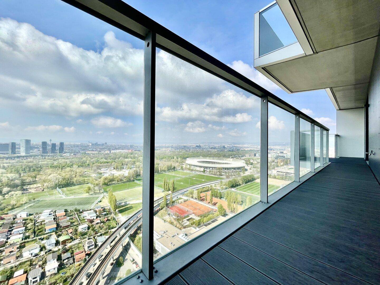 Geräumiger Balkon mit Glasgeländer und weitem Blick über die Stadt und das Stadion.