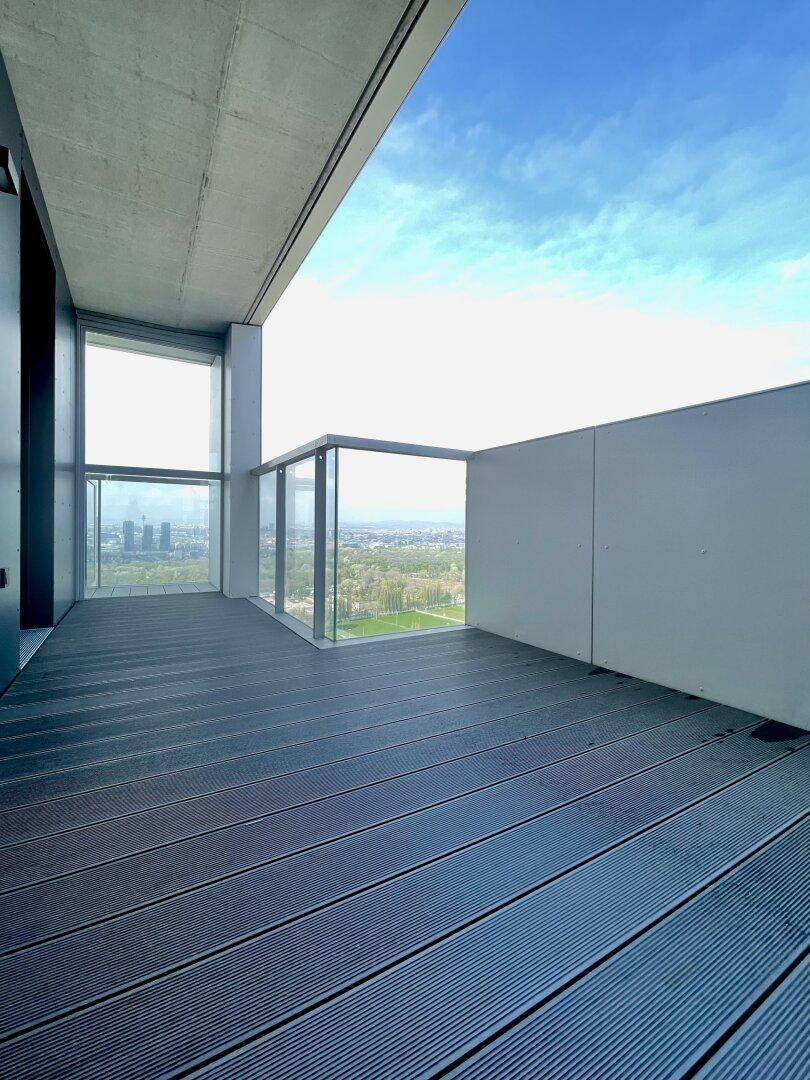 Großer Balkon mit modernem Glasgeländer und weitem Blick über die grüne Umgebung.
