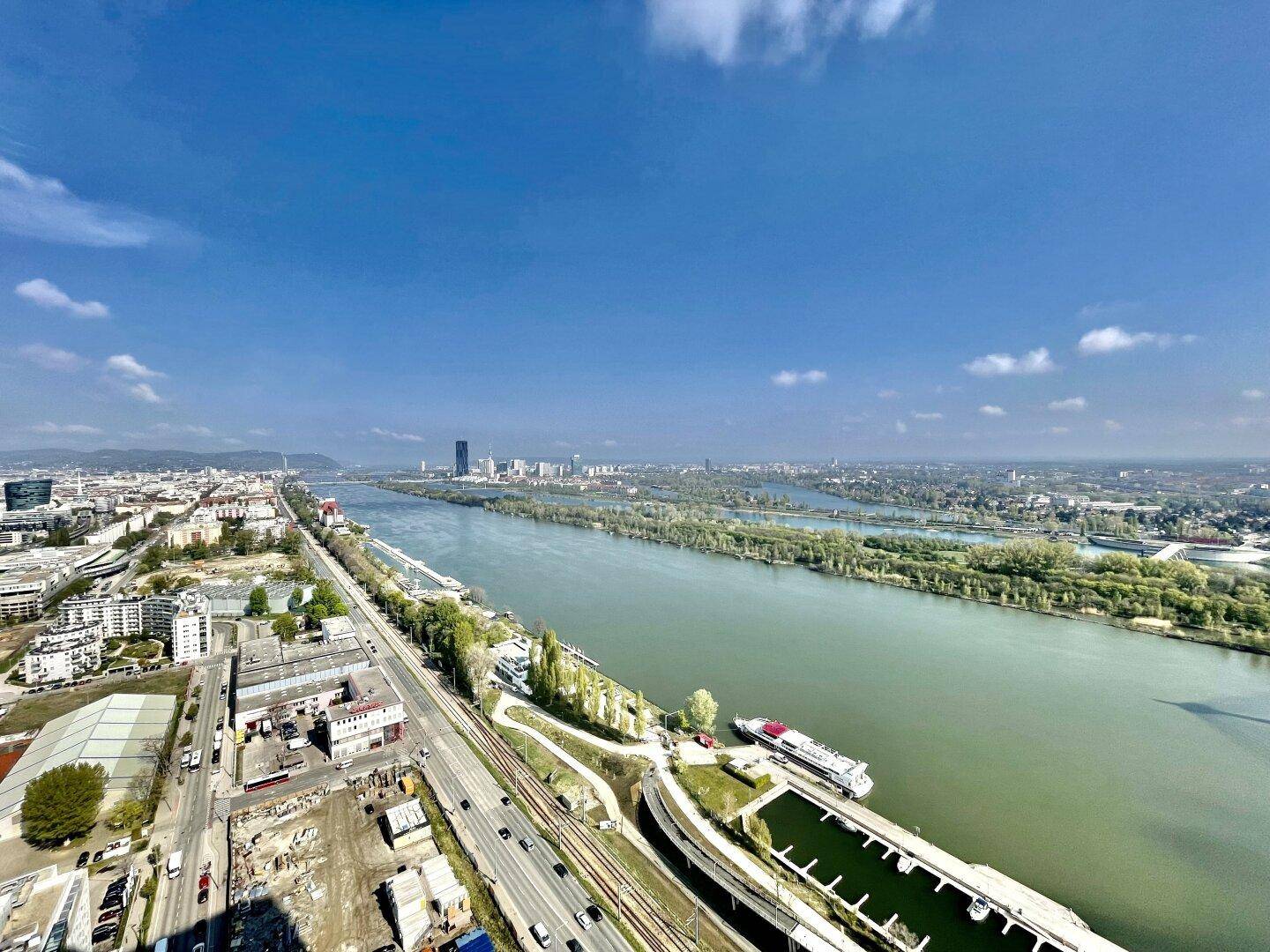 Weitläufiger Blick über die Donau und die Skyline der Stadt unter einem klaren blauen Himmel.