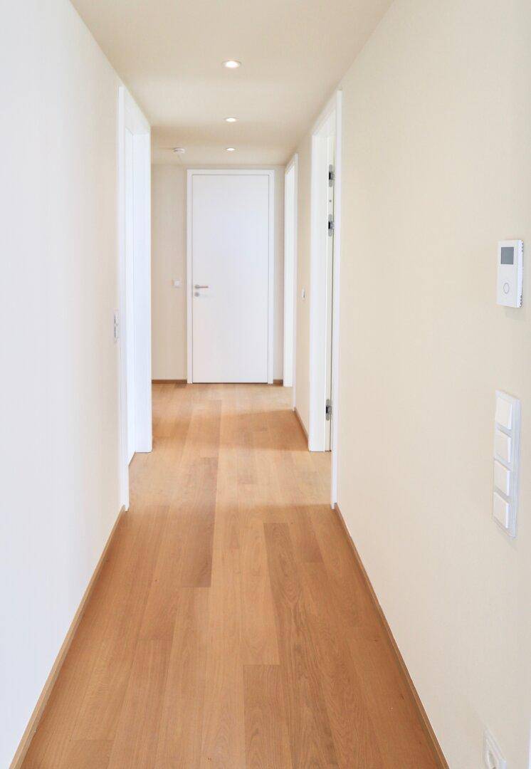 Langer, heller Flur mit Holzboden und modernen Lichtelementen, der die Wohnbereiche verbindet.