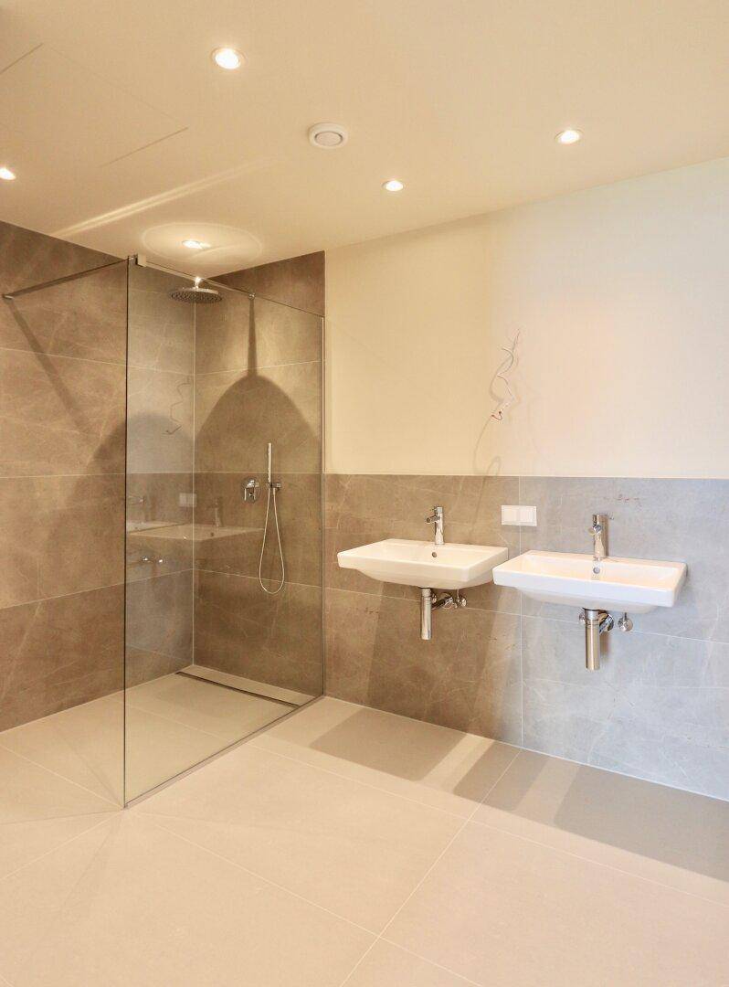 Modernes Badezimmer mit doppelten Waschbecken, großer begehbarer Dusche und eleganten Fliesen.