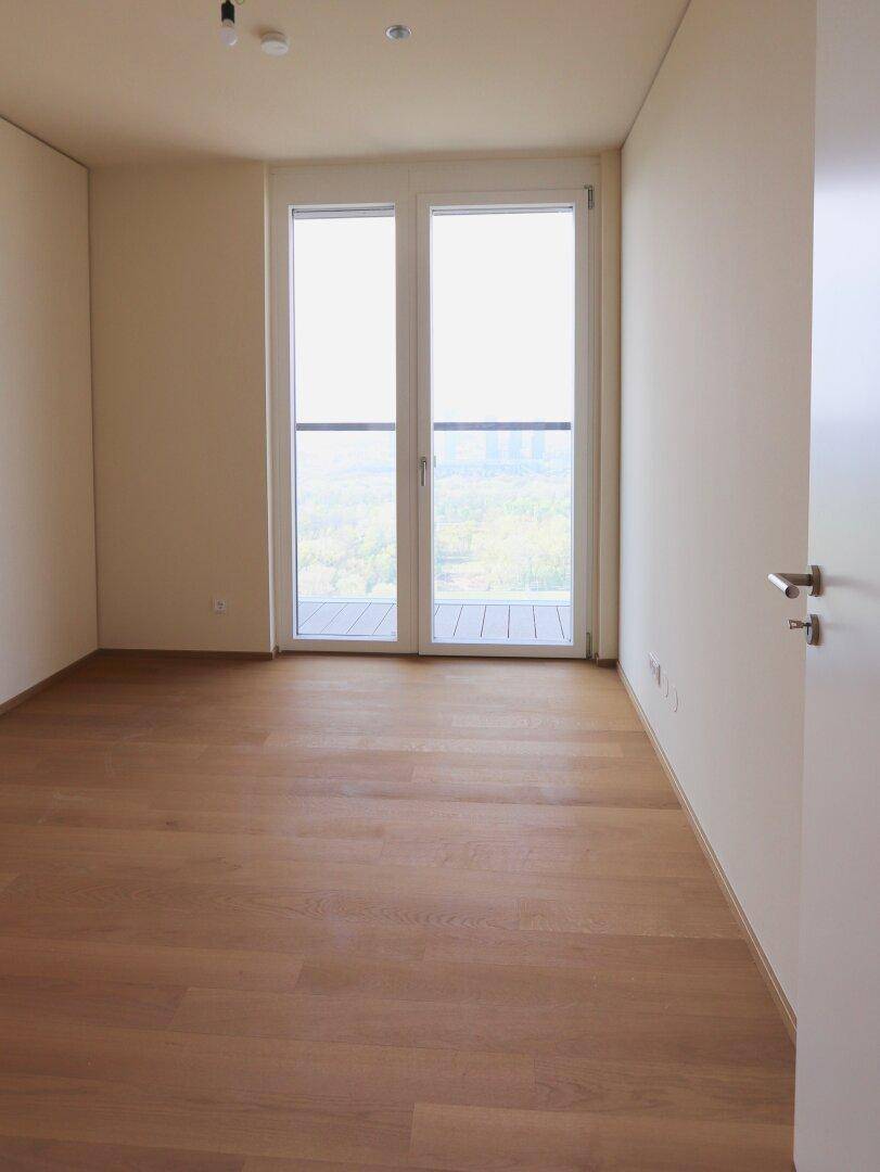 Helles Schlafzimmer mit Holzboden und Zugang zu einem Balkon, ideal für natürliche Belichtung.