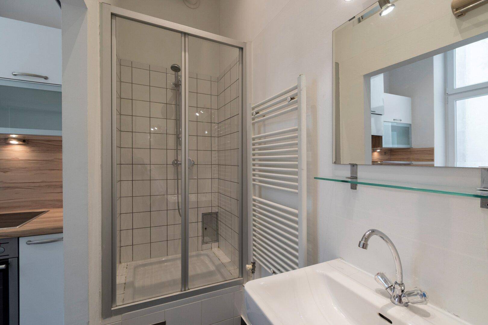 Modernes Badezimmer mit Duschkabine, Waschbecken und beheiztem Handtuchhalter.
